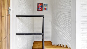 Una escalera estrecha con barandilla negra, paredes de ladrillo blanco y suelo de madera.