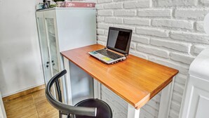Una habitación pequeña con un escritorio de madera, una computadora portátil, una silla y una pared de ladrillo blanco.