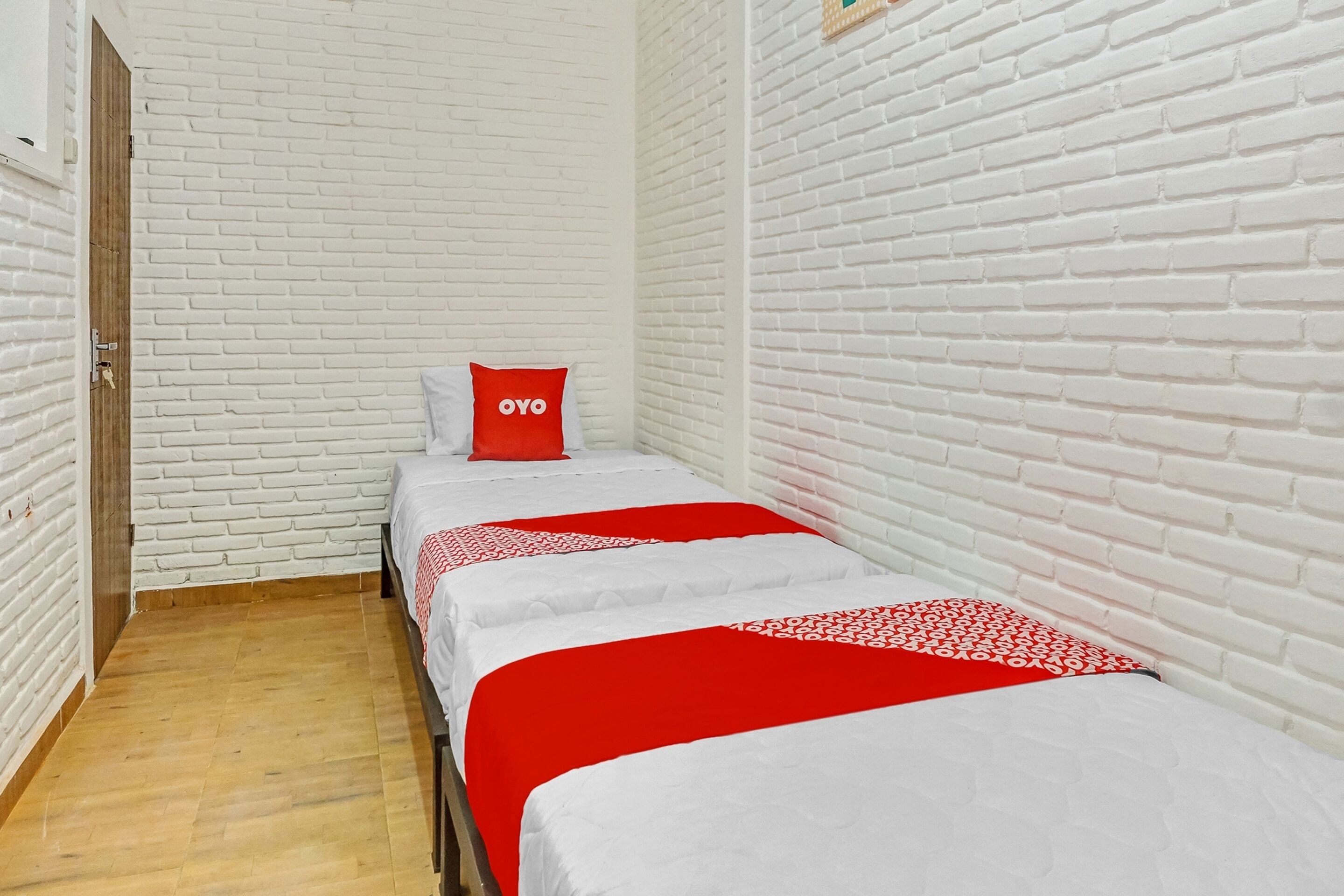 Une pièce aux murs en briques blanches, avec un plancher en bois et deux lits recouverts de draps rouges et blancs.