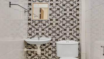 Un baño con pared de azulejos estampados, un lavamanos, un inodoro y una ventana sobre el lavamanos.