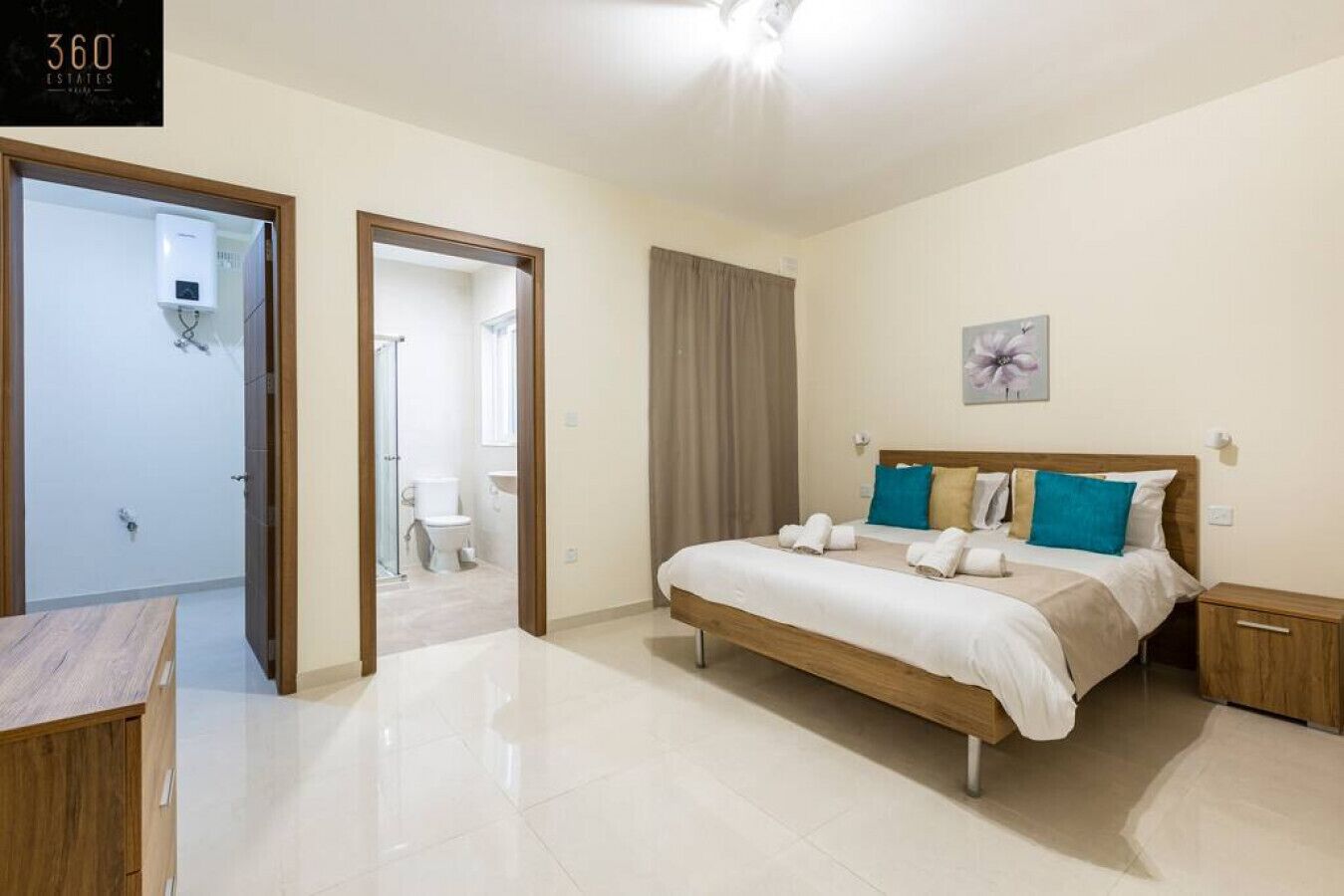 Une chambre moderne avec un grand lit, des tables de chevet, une salle de bain visible à travers une porte ouverte et un luminaire au plafond.
