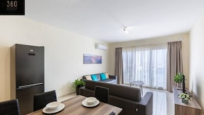 Een moderne woonkamer met een bank, een eettafel met borden, een zwarte koelkast en een raam met gordijnen.