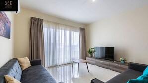 Een moderne woonkamer met twee banken, een salontafel, een televisie en een groot raam met gordijnen.