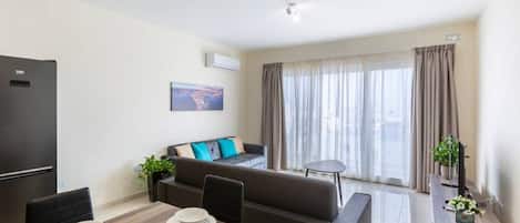 A modern living room with a sofa, a dining table with plates, a black refrigerator, and a window with curtains.