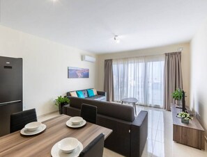Una sala de estar moderna con un sofá, una mesa de comedor con platos, un refrigerador negro y una ventana con cortinas.