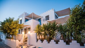 A white building with a sign reading 'Pico Bello' and a courtyard with a table, chairs, and plants. - Apartment In A Hotel 'Pico Bello Patmos 22' with Mountain View, Wi-Fi and Air Conditioning (Patmos)