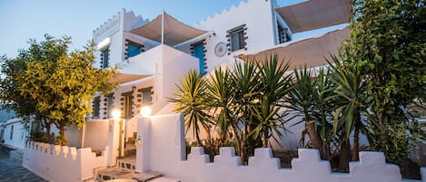 A white building with a sign reading 'Pico Bello' and a courtyard with a table, chairs, and plants.