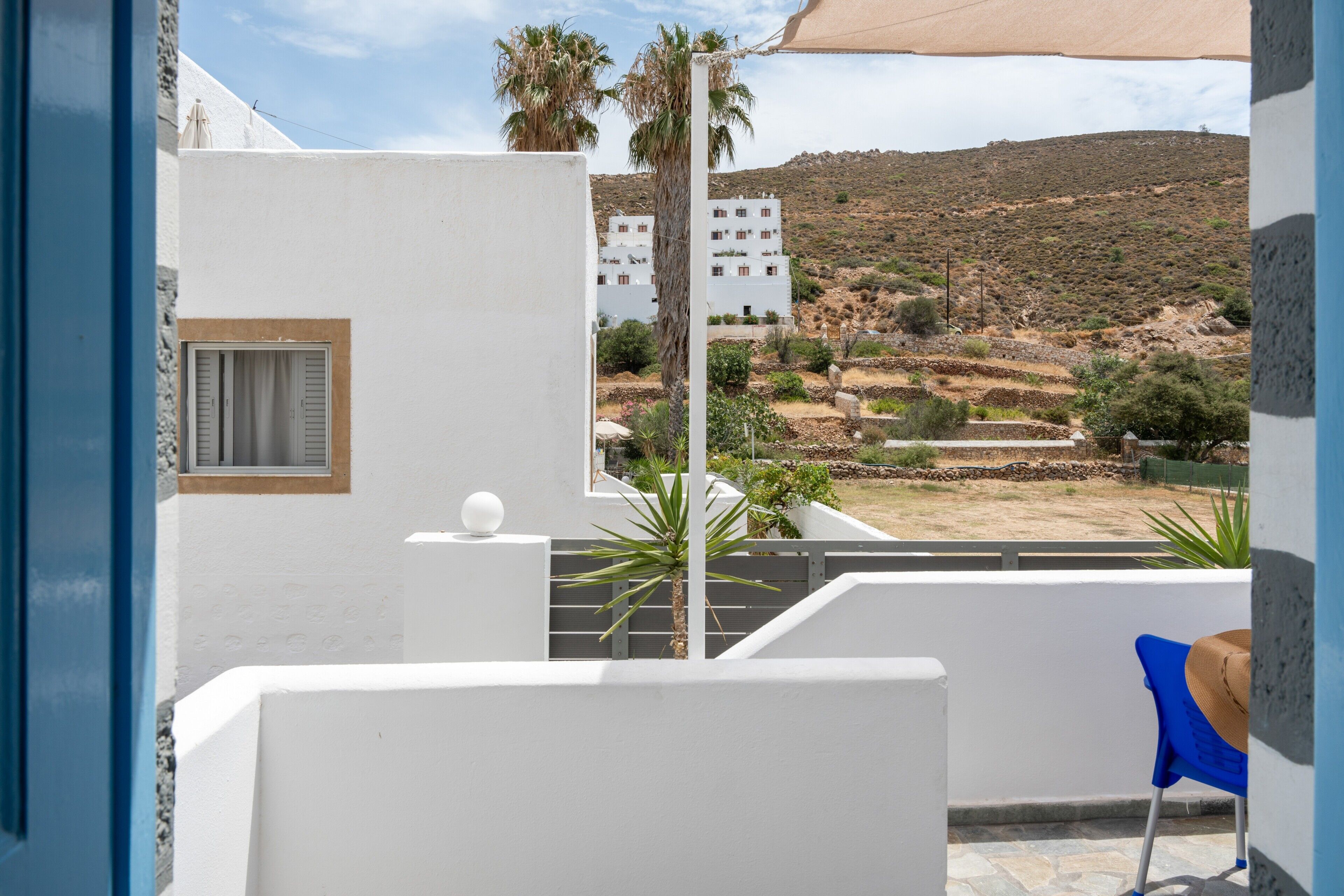 A white building with a balcony, a blue chair, and a view of a hilly landscape.