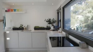 A modern kitchen with white cabinetry, a black countertop, and a large window offering a view of greenery outside. - Superbe Maison 1min Plage (Sausset-les-Pins)