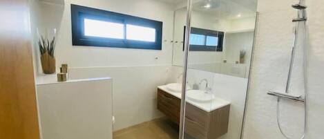 A modern bathroom with a glass shower enclosure, a white sink, and a wooden vanity.