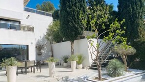 A modern outdoor patio with a seating area, potted plants, and a staircase leading to an upper level. - Superbe Maison 1min Plage (Sausset-les-Pins)