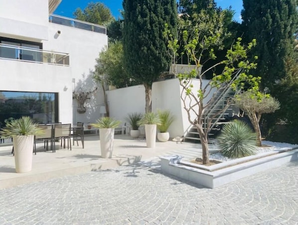 A modern outdoor patio with a seating area, potted plants, and a staircase leading to an upper level.