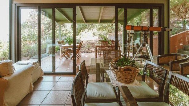 A spacious indoor area with a large sliding glass door leading to an outdoor patio. Inside, there is a sofa, a dining table with chairs, and a telescope on a stand. - Country House in Gran Canaria with Private Pool (San Mateo)