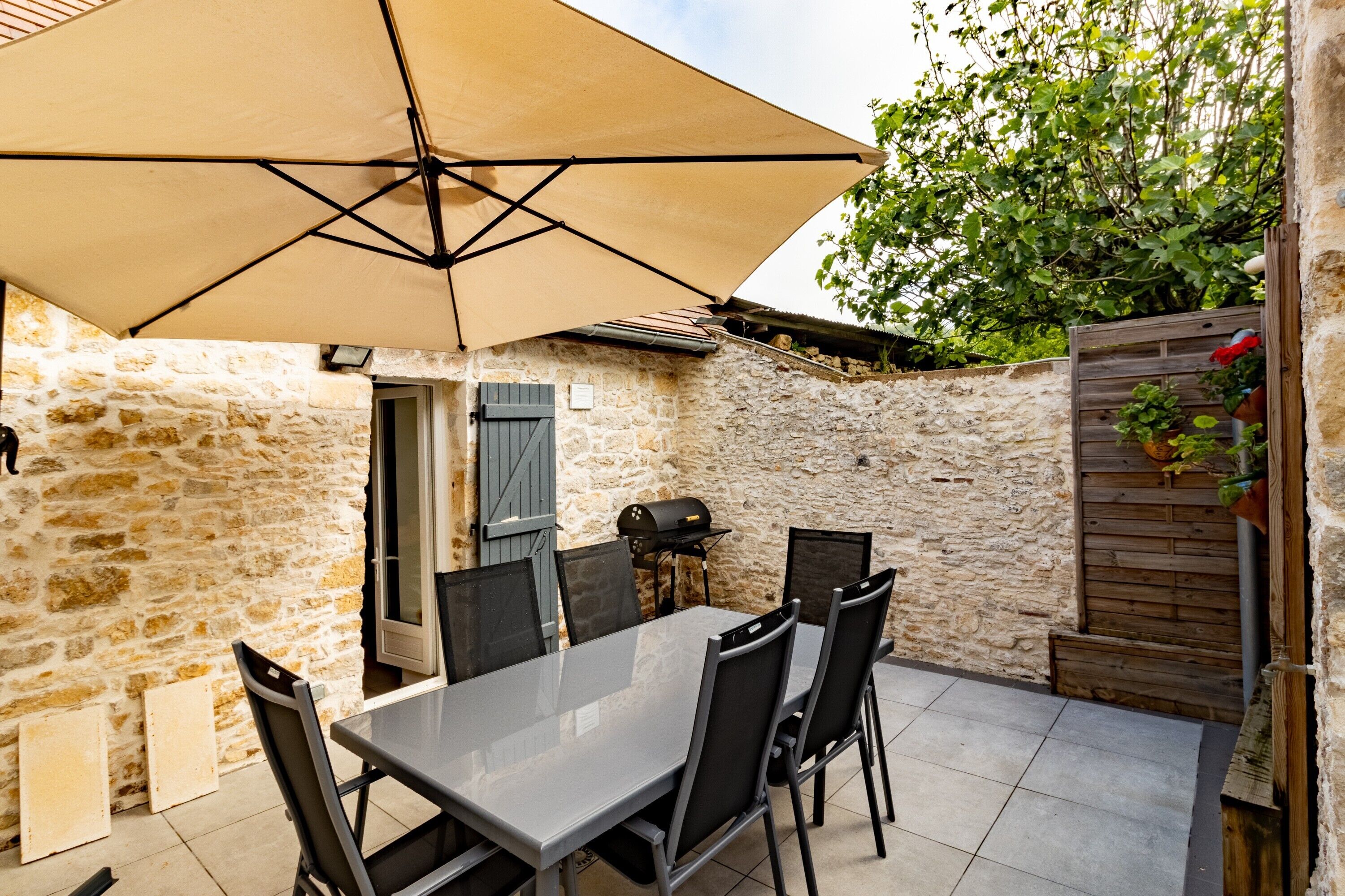 Eine Terrasse mit Steinwänden, einem Tisch, Stühlen, einem Sonnenschirm und einem Grill.