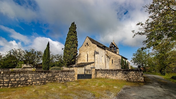 En historisk kyrka byggd av sten, med ett klocktorn, omgiven av stenmurar och en grusgång.