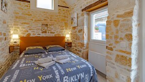 A room with a stone wall, a bed with a headboard, a window, and a wall-mounted light fixture. - Holiday Home 'La Boutique Germain 4 to 6 Persons' with Private Terrace (Lacave)