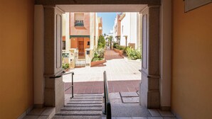 A corridor leading to a courtyard with a gate, steps, and a view of buildings in the distance.