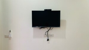 A flat-screen TV mounted on a white wall with a power outlet and a thermostat below it. - Suanvadee Resort (Koh Samui)