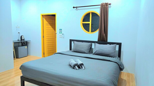 A bedroom with a bed, a desk, a chair, a small table, a wall-mounted clock, and a door. - Suanvadee Resort (Koh Samui)