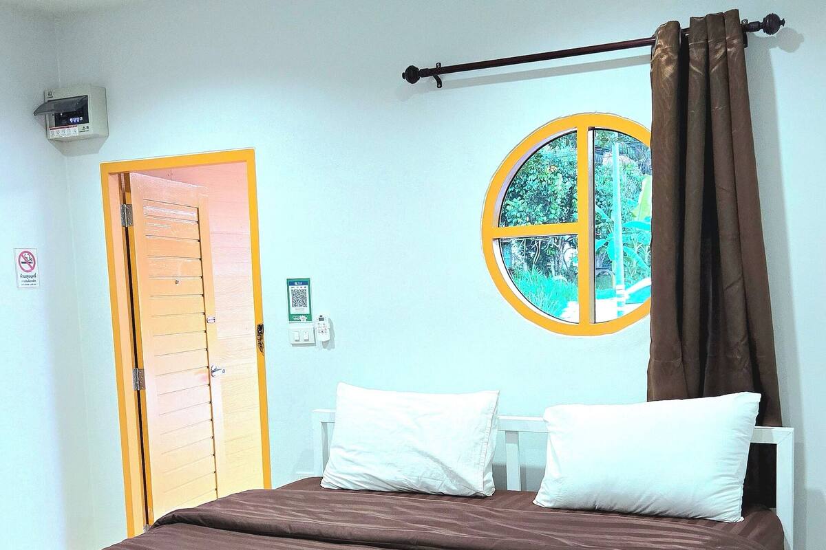 Una camera d'albergo con un letto, una finestra con tende, una porta e un condizionatore d'aria a parete.
