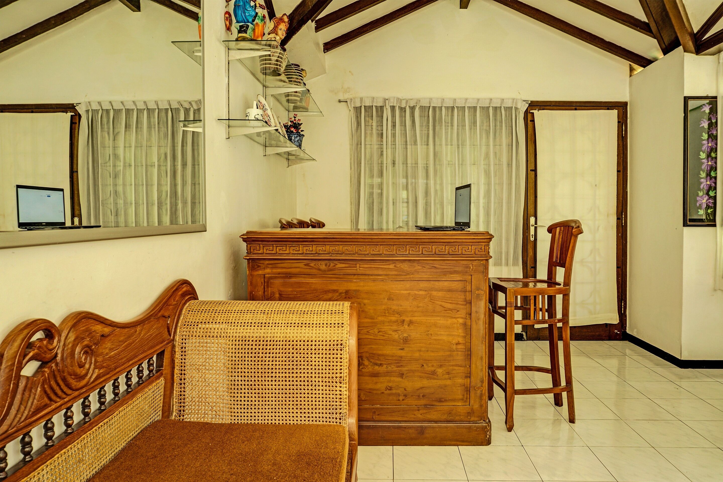 A room with a wooden desk, a wicker sofa, a wooden chair, and a computer on the desk.