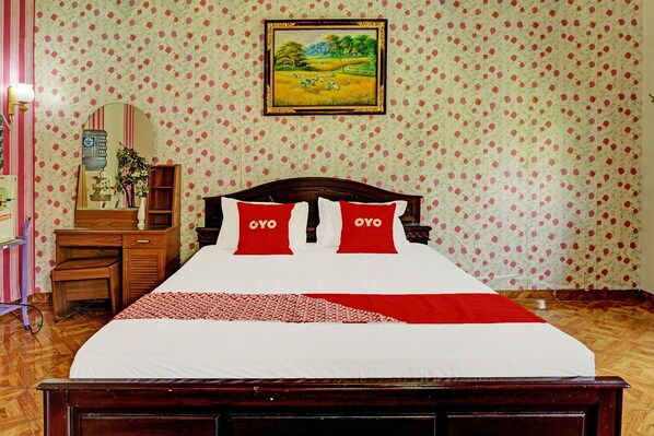 Un lit bien fait, avec une literie rouge et blanche, une tête de lit en bois et un motif de papier peint floral.