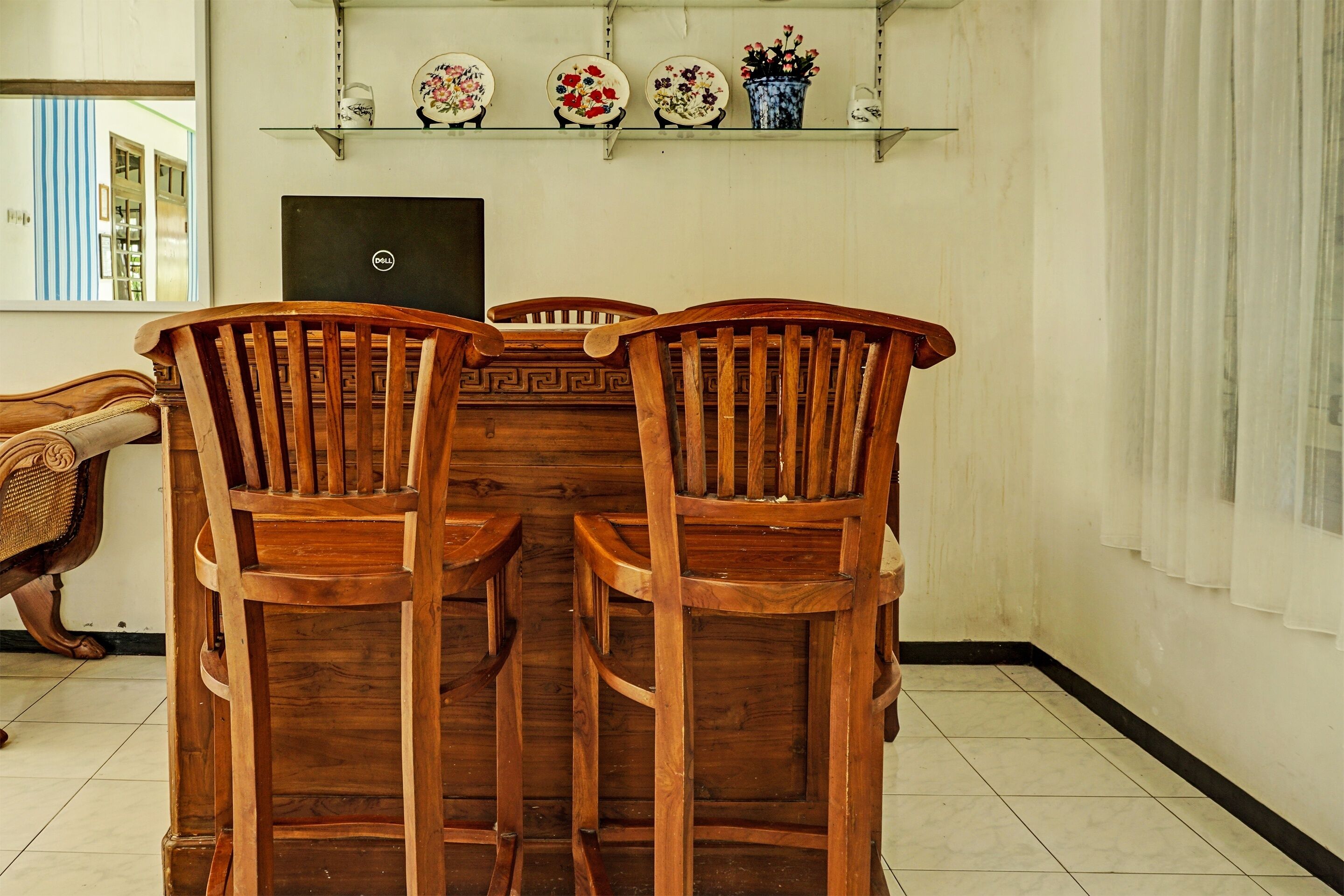 A dining area with a wooden table and chairs, a laptop on the wall, and decorative plates on shelves.