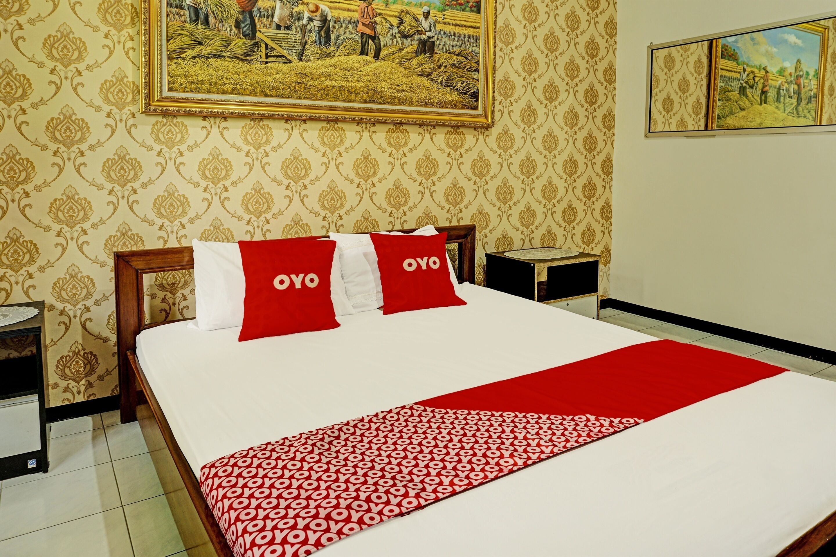 A hotel room with a large bed, two nightstands, a red and white patterned throw, and two pillows with the text "OYO".