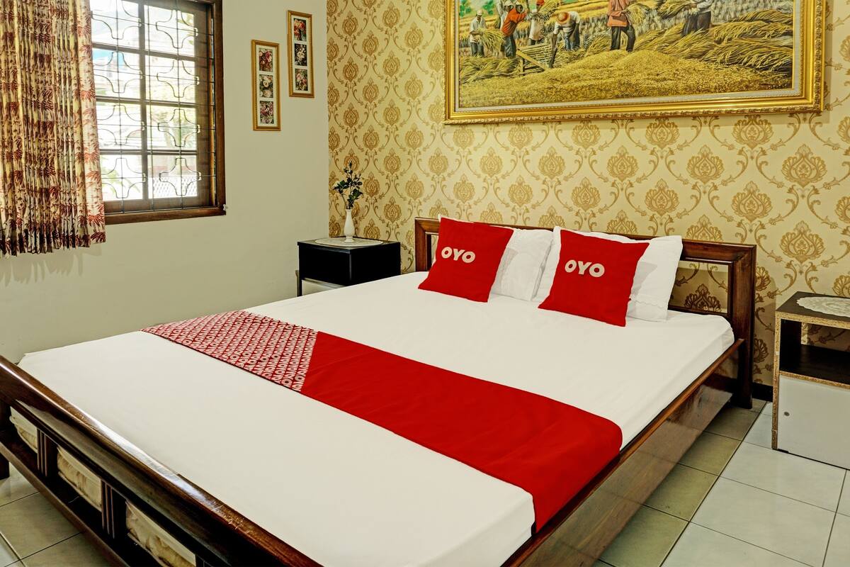 Quarto de hotel com uma cama grande, mesa de cabeceira, quadro na parede e janela com cortinas.