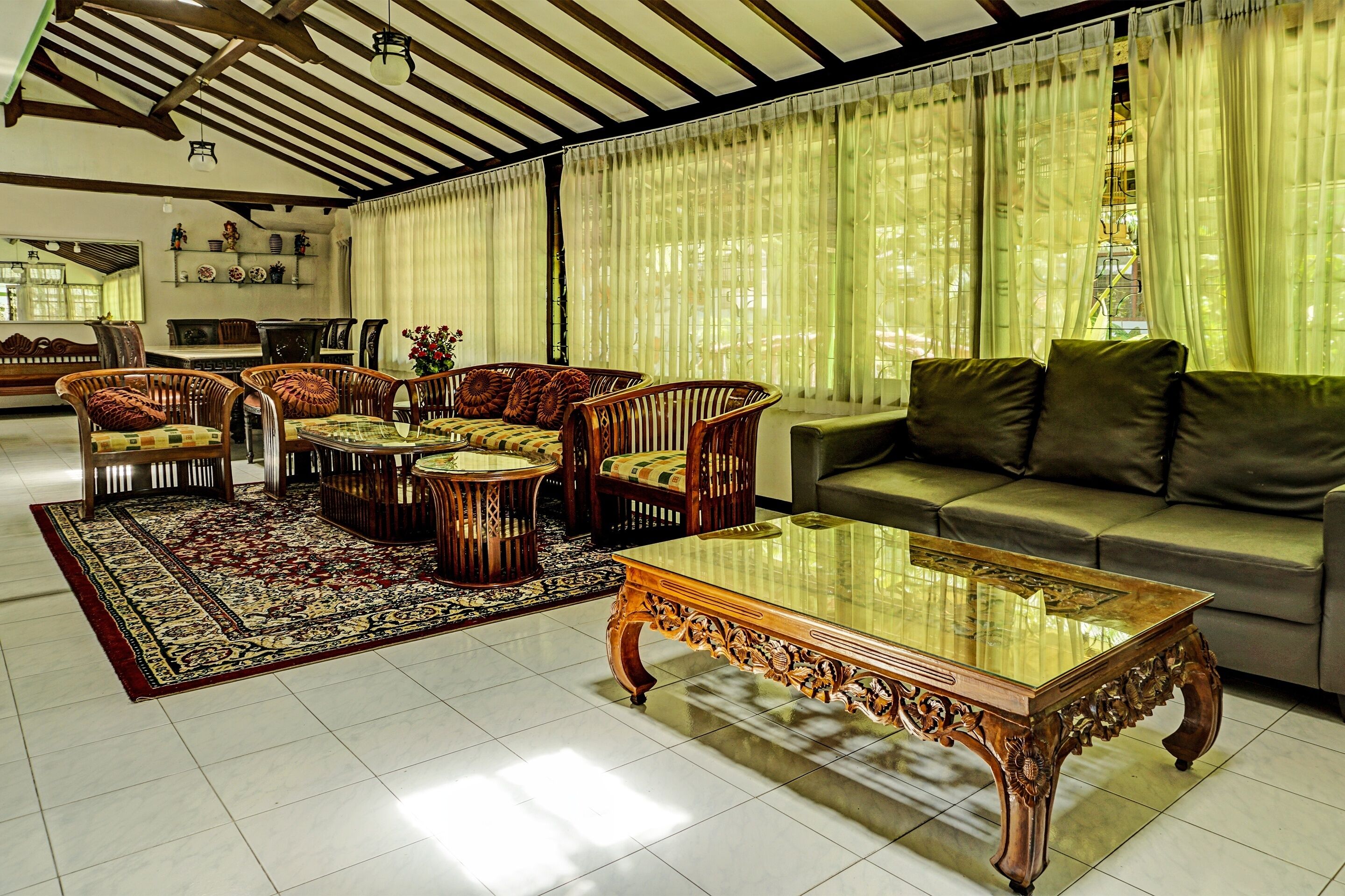 A spacious living room with a large glass coffee table, wicker chairs, a sofa, and a patterned rug.