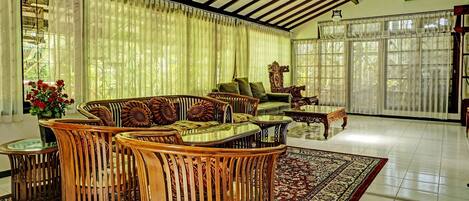 Un salón espacioso con techo alto, ventanas grandes y un conjunto de sofá de madera estilo tradicional.