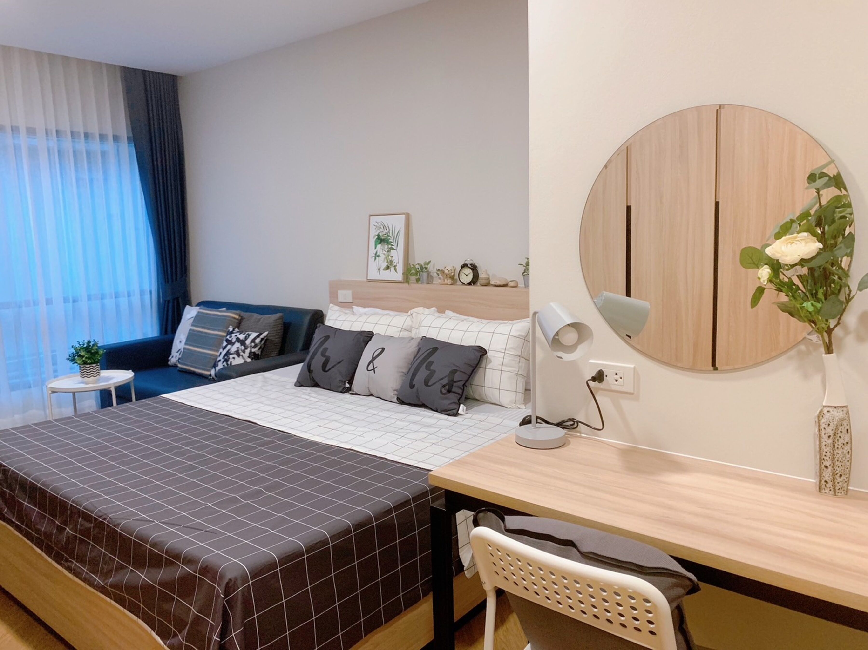 Um quarto moderno com uma cama, uma escrivaninha, uma cadeira, um espelho redondo e uma pequena mesa com uma planta.
