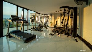 A modern gym with a treadmill, elliptical, and various exercise machines, large windows, and a fan. - Increase Hotel&residence (Bang Phli)