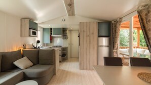 A modern kitchen with built-in appliances, a dining area with a table and chairs, and a living room with a sofa and a lamp. - Mobile Home "Les Pieds Dans L'Eau" with Private Terrace, Private Garden & A/C (Canet-en-Roussillon)
