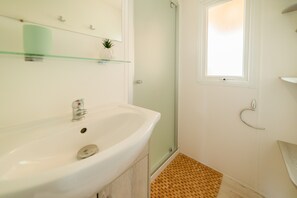 Un baño con lavamanos blanco, repisa de vidrio y zona de ducha.
