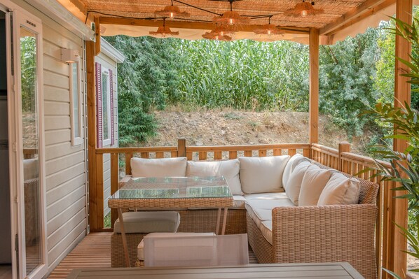 Un espacio al aire libre cubierto con sofá y mesa de mimbre, terraza de madera y vista a un campo de maíz.