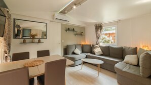A modern living room with a sofa, a dining table, and a coffee table. - Mobile Home "Les Pieds Dans L'Eau" with Private Terrace, Private Garden & A/C (Canet-en-Roussillon)