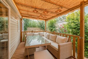 Un espace extérieur aménagé avec une zone salon couverte, dotée d'une table à plateau en verre, d'un canapé en osier et d'une terrasse en bois.