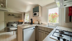 A compact kitchen with a dishwasher, microwave, and gas stove. - Mobile Home "Les Pieds Dans L'Eau" with Private Terrace, Private Garden & A/C (Canet-en-Roussillon)