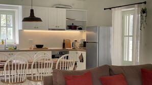 Eine moderne Küche mit weißen Schränken, einem eingebauten Ofen und einem Edelstahl-Kühlschrank. Es gibt eine Essecke mit einem Holztisch und weißen Stühlen.