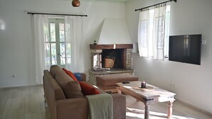 Ein Wohnzimmer mit einer Couch, Hocker, Kamin und einem an der Wand befestigten Flachbildfernseher.