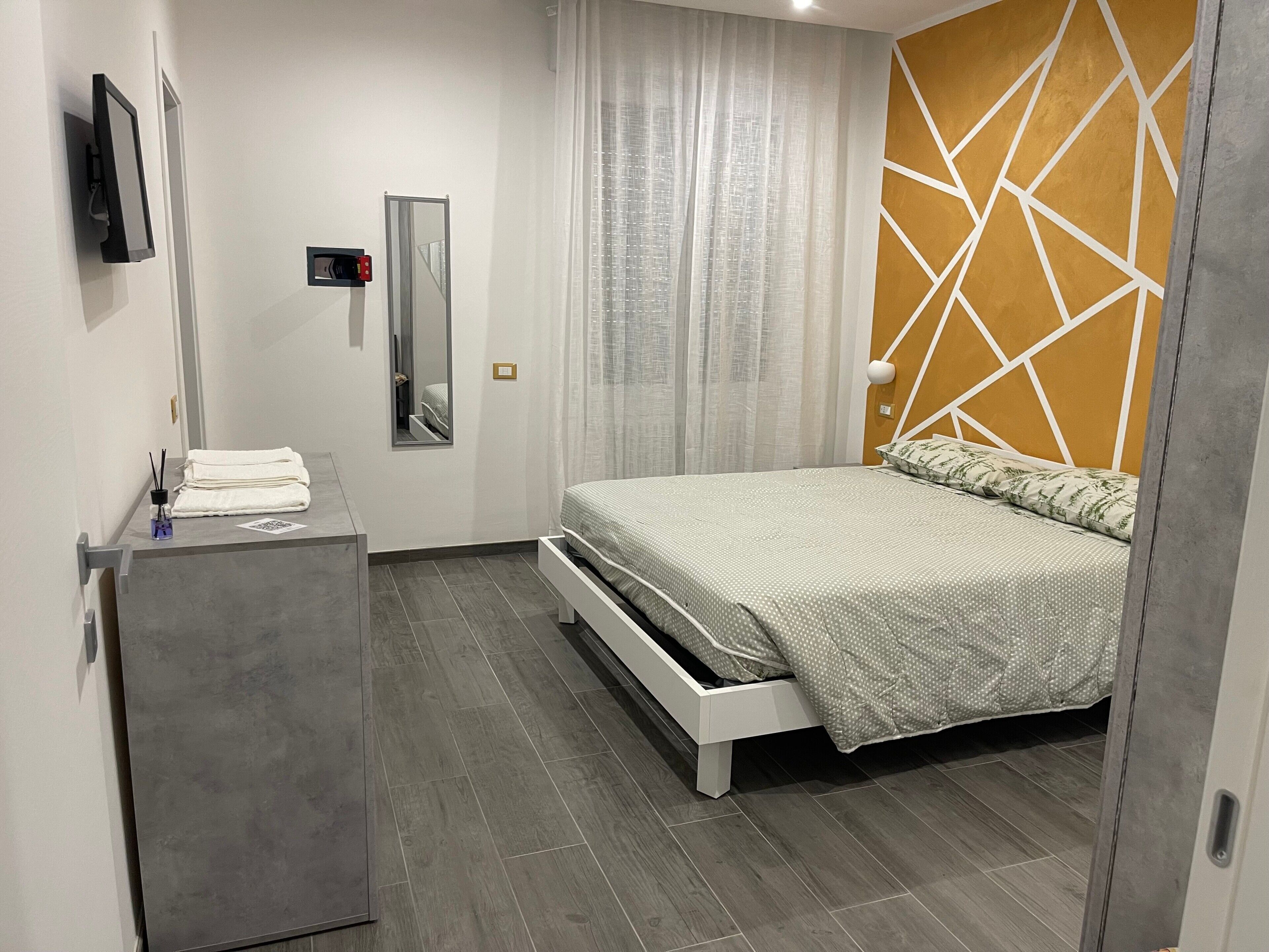 Ein Schlafzimmer mit einem Bett, einem Nachttisch, einem Spiegel, einem Kleiderschrank und einem an der Wand befestigten Fernseher.
