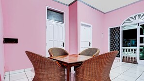 Une pièce avec un mur rose, une table en bois et quatre chaises en osier, ainsi qu’une porte blanche dotée d’une fenêtre.
