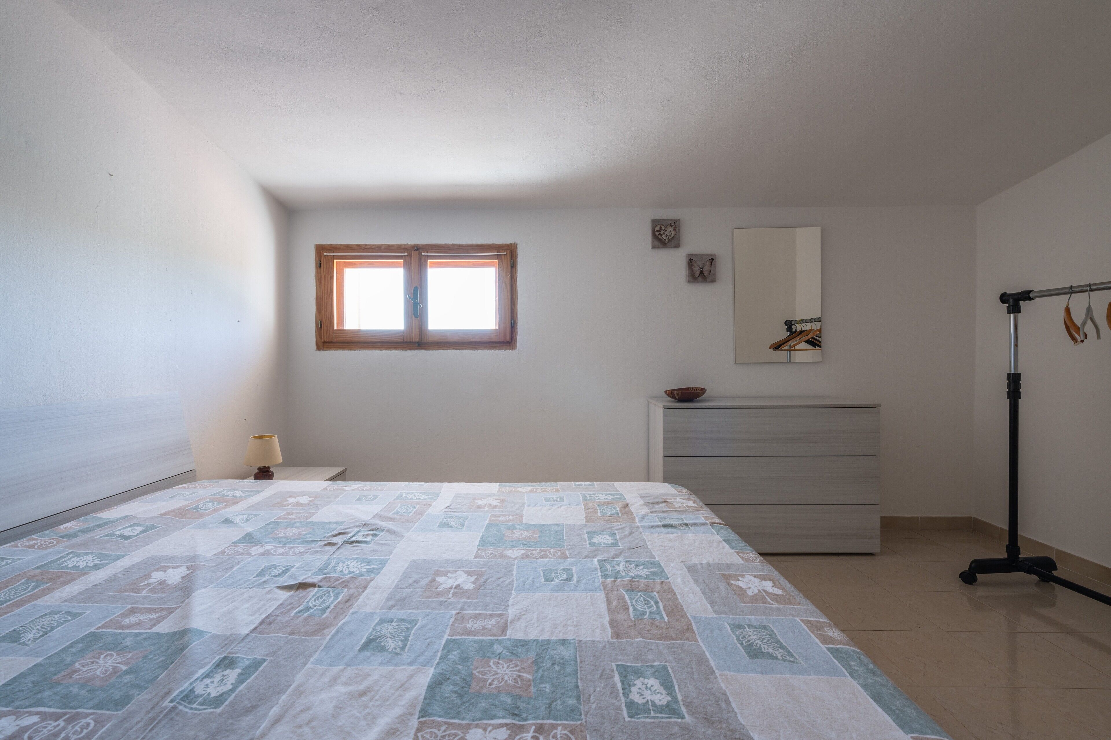 A bedroom with a bed, a dresser, a mirror, a window, and a lamp.