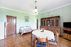 Un área de comedor con una mesa redonda, sillas, un aparador con trofeos, un sofá y una televisión.