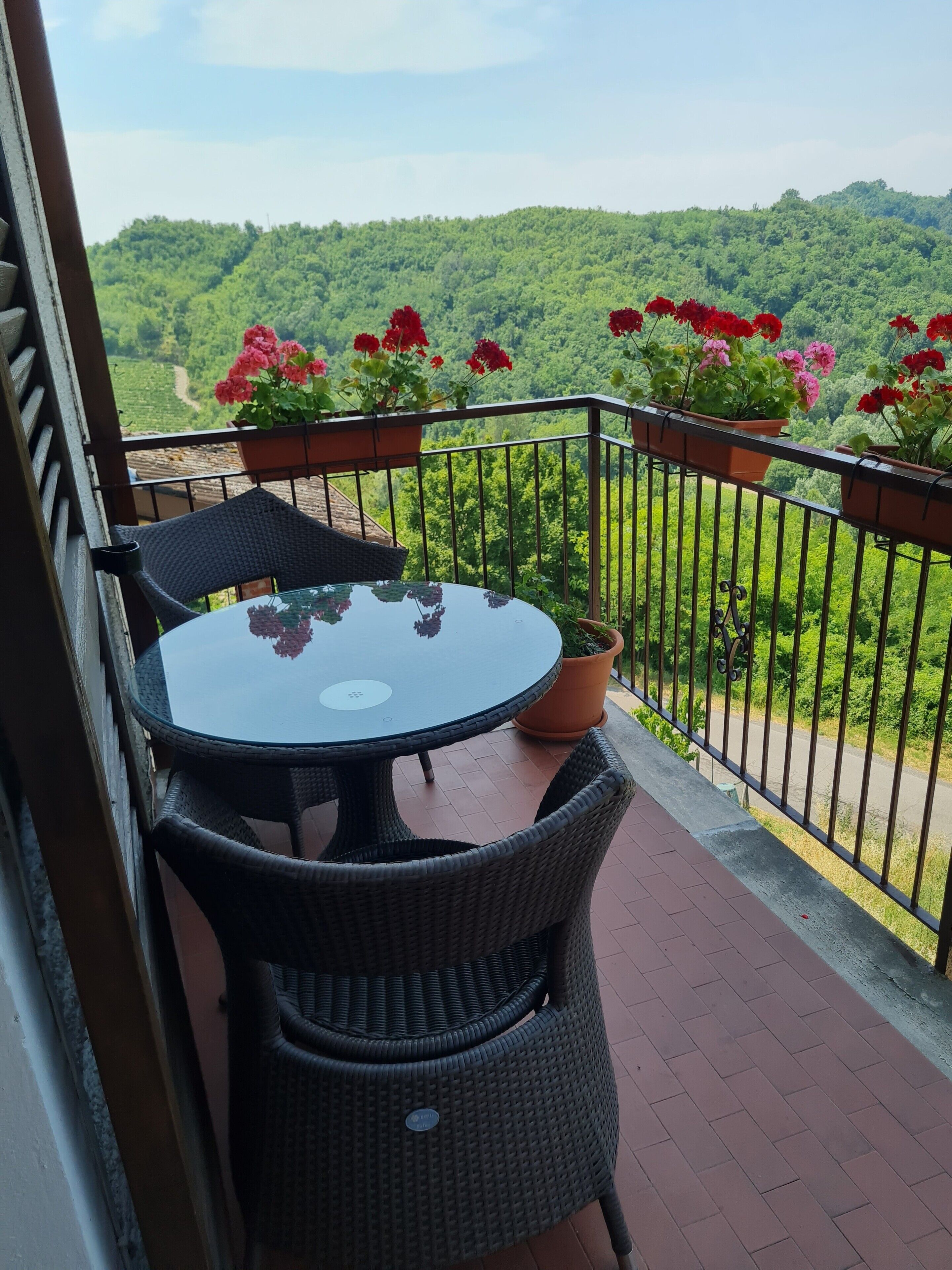 A balcony with a round table and wicker chairs, overlooking a lush green landscape.