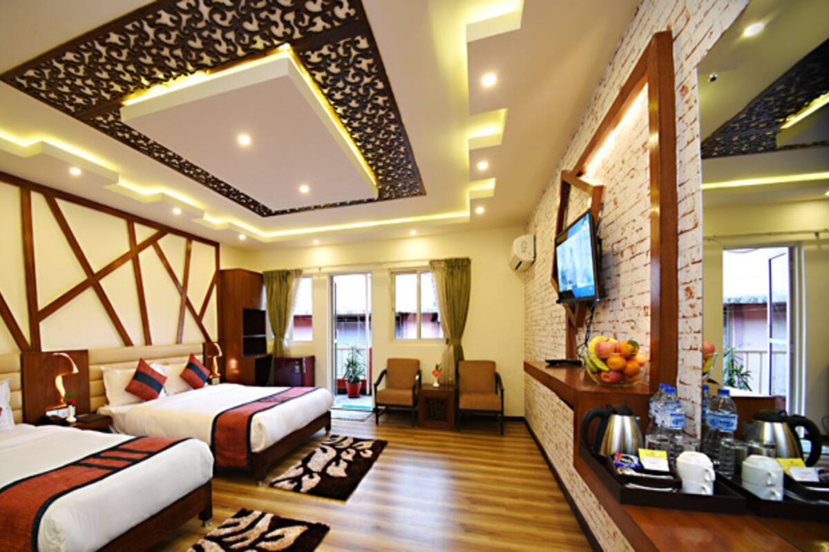 A hotel room with two beds, a wooden wardrobe, a desk with a computer, and a TV mounted on the wall.
