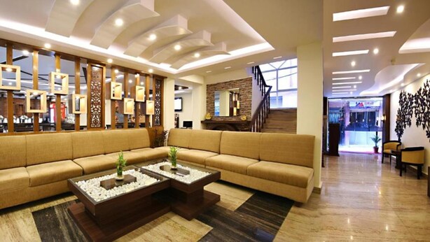 A modern hotel lobby with a large beige sofa, a coffee table, and a decorative wall with framed pictures. - MeroStay 172 Hotel JP (Kathmandu)