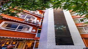 A multi-story building with balconies, a central vertical feature, and a tree in the foreground. - MeroStay 172 Hotel JP (Kathmandu)