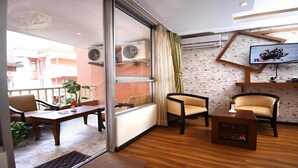 A modern living room with a glass door leading to a balcony, a flat-screen TV mounted on a brick wall, and a wooden coffee table. - MeroStay 172 Hotel JP (Kathmandu)